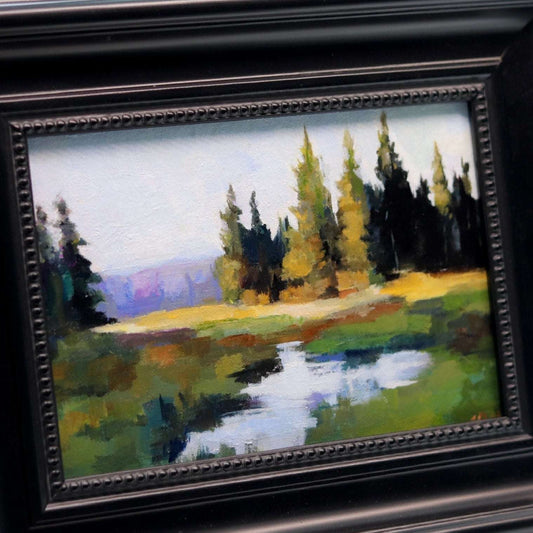 Framed painting of a landscape with trees and a stream.