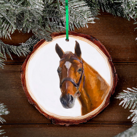 a painted ornament of a brown horse is on table with pine and green ribbon